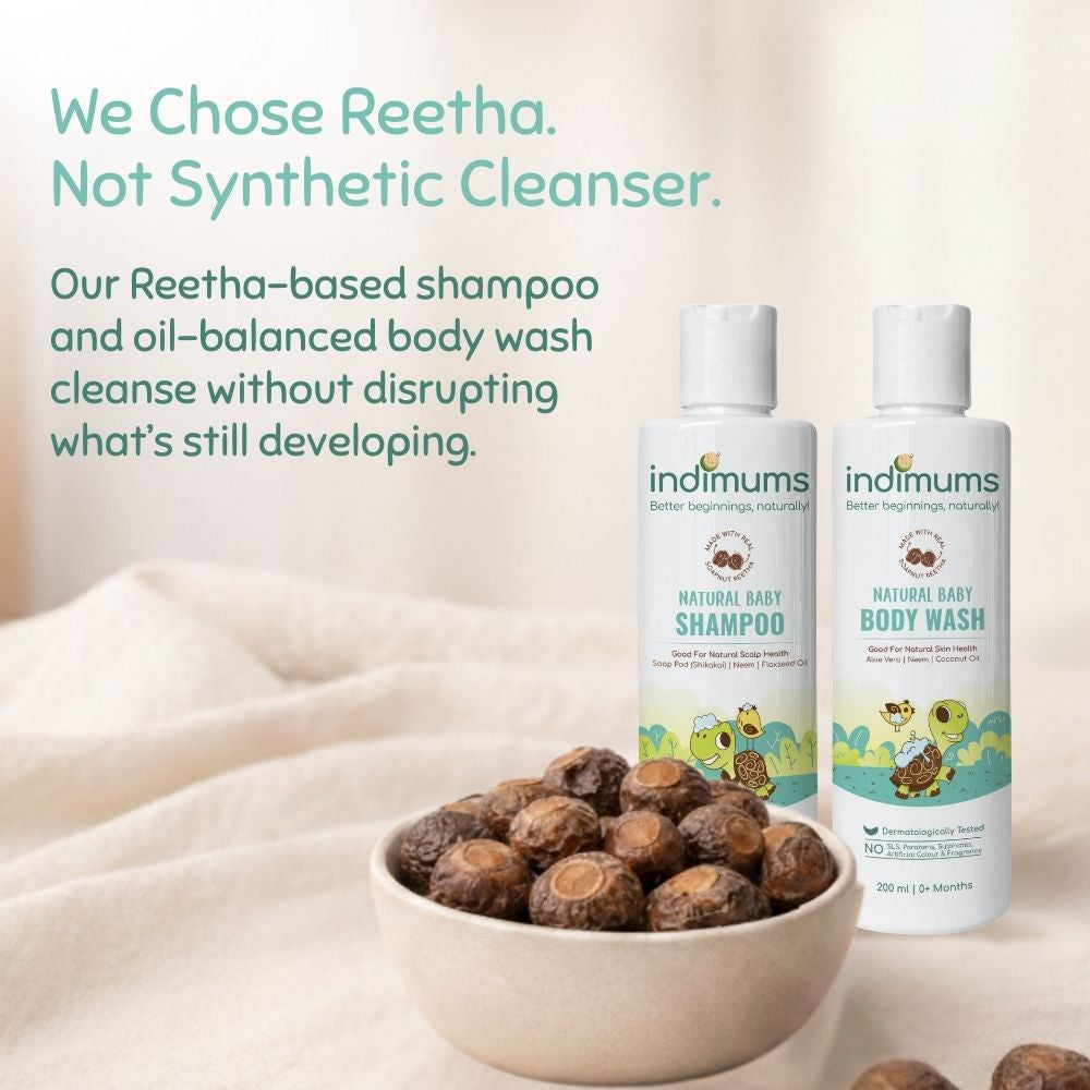 Two bottles of Indimums natural baby shampoo and body wash with a bowl of Reetha fruits on a light background.