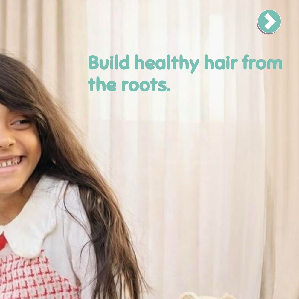 Child with long hair smiling in front of a beige curtain with text 'Build healthy hair from the roots.'